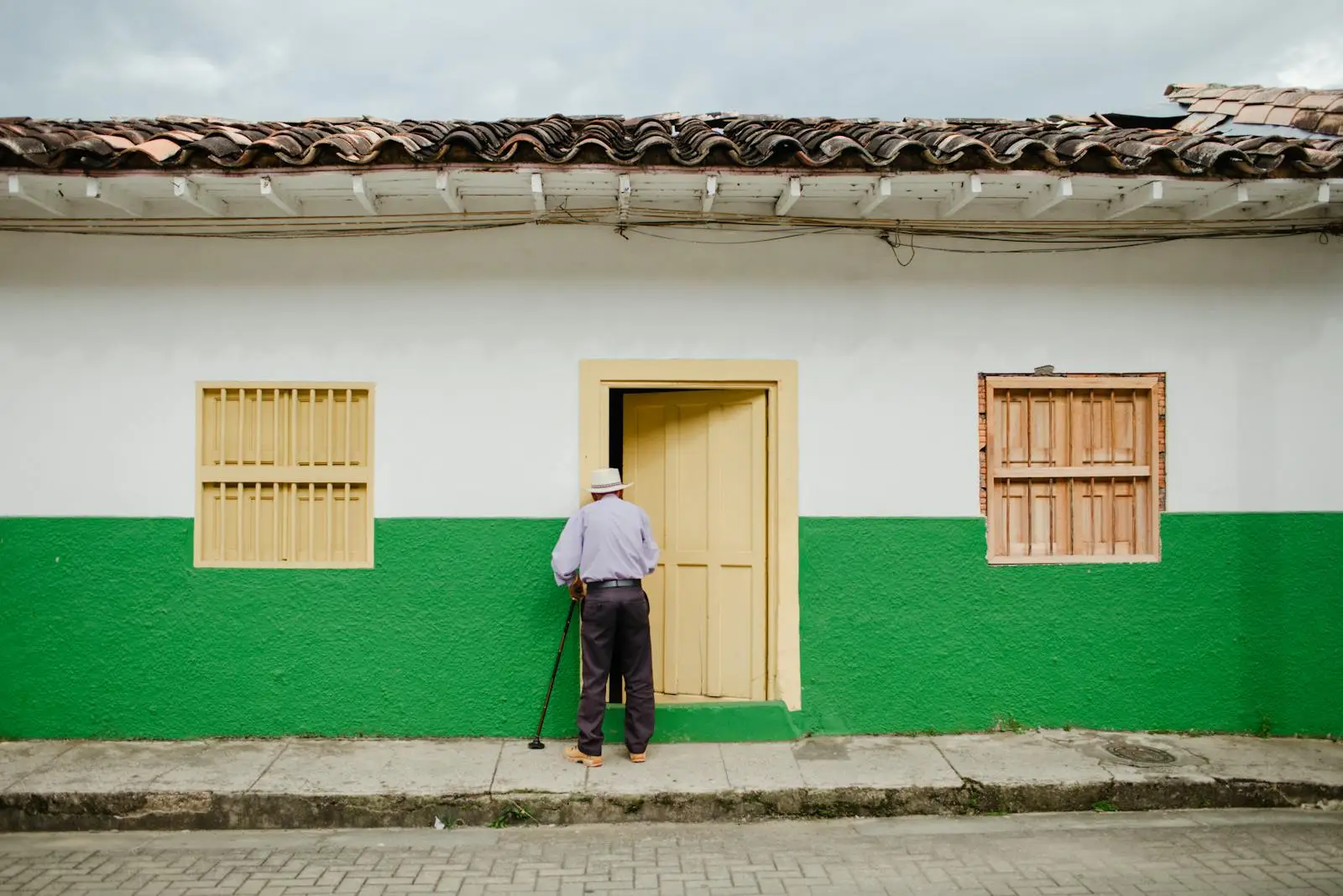An elderly man stands by a colorful traditional house in Jericó, Colombia.